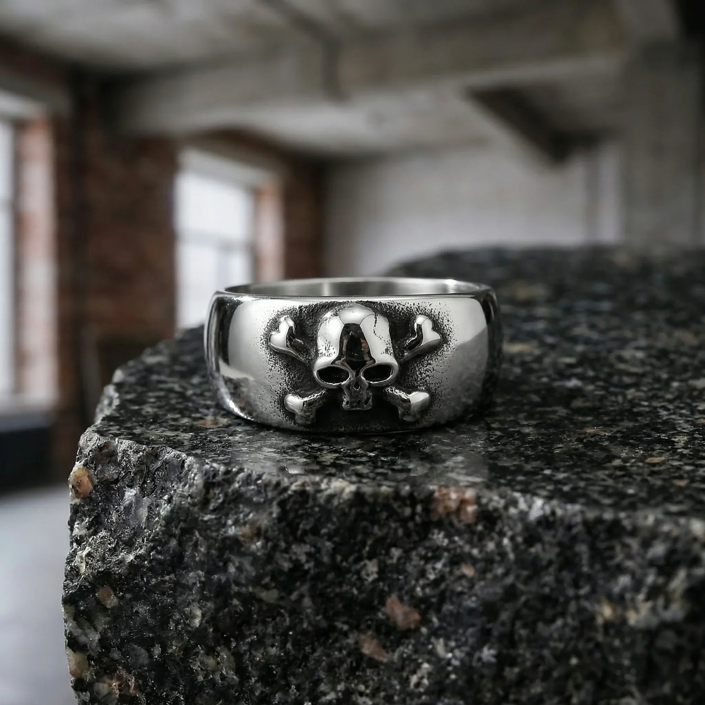Men’s silver skull ring with crossbones design on textured stone surface