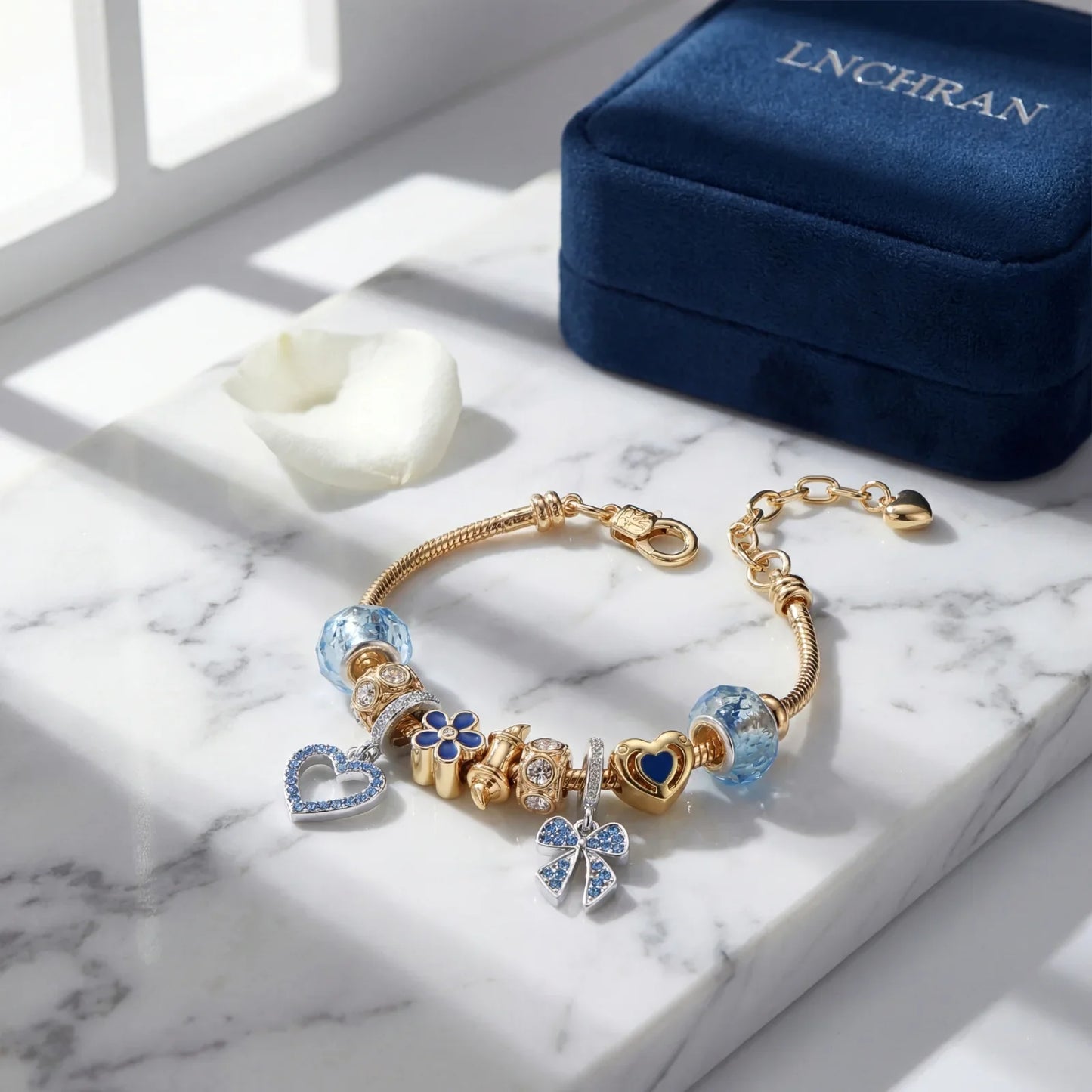 Gold charm bracelet with blue and heart-shaped accents on marble, elegant jewelry display.
