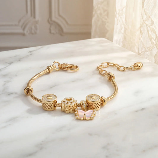 Gold charm bracelet with diamond accents and pink butterfly, displayed on marble surface