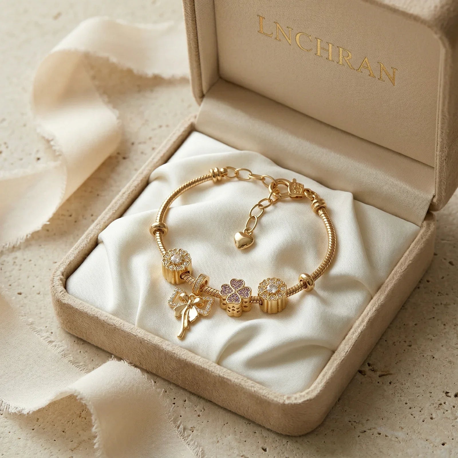 Gold charm bracelet with floral and heart designs in a beige jewelry box on satin fabric