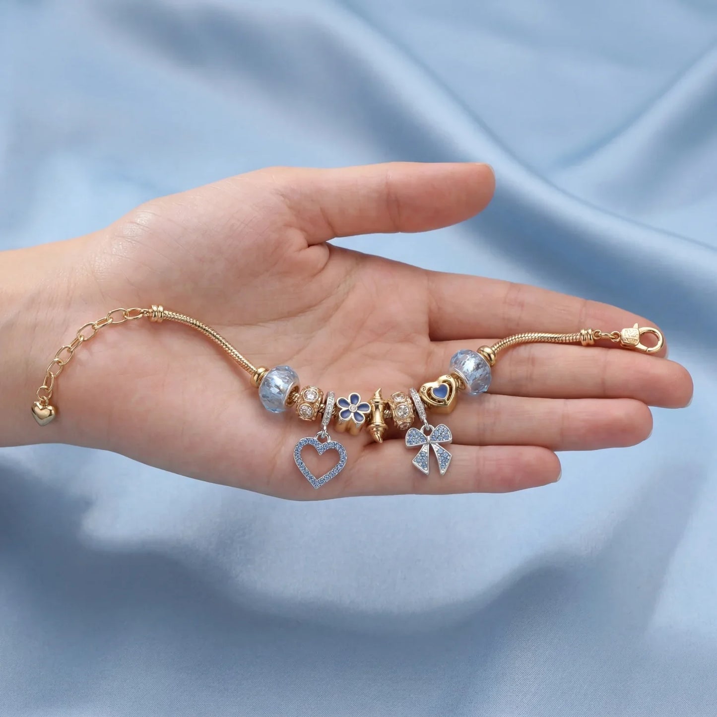 Gold charm bracelet with heart, flower, and bow pendants displayed on a hand