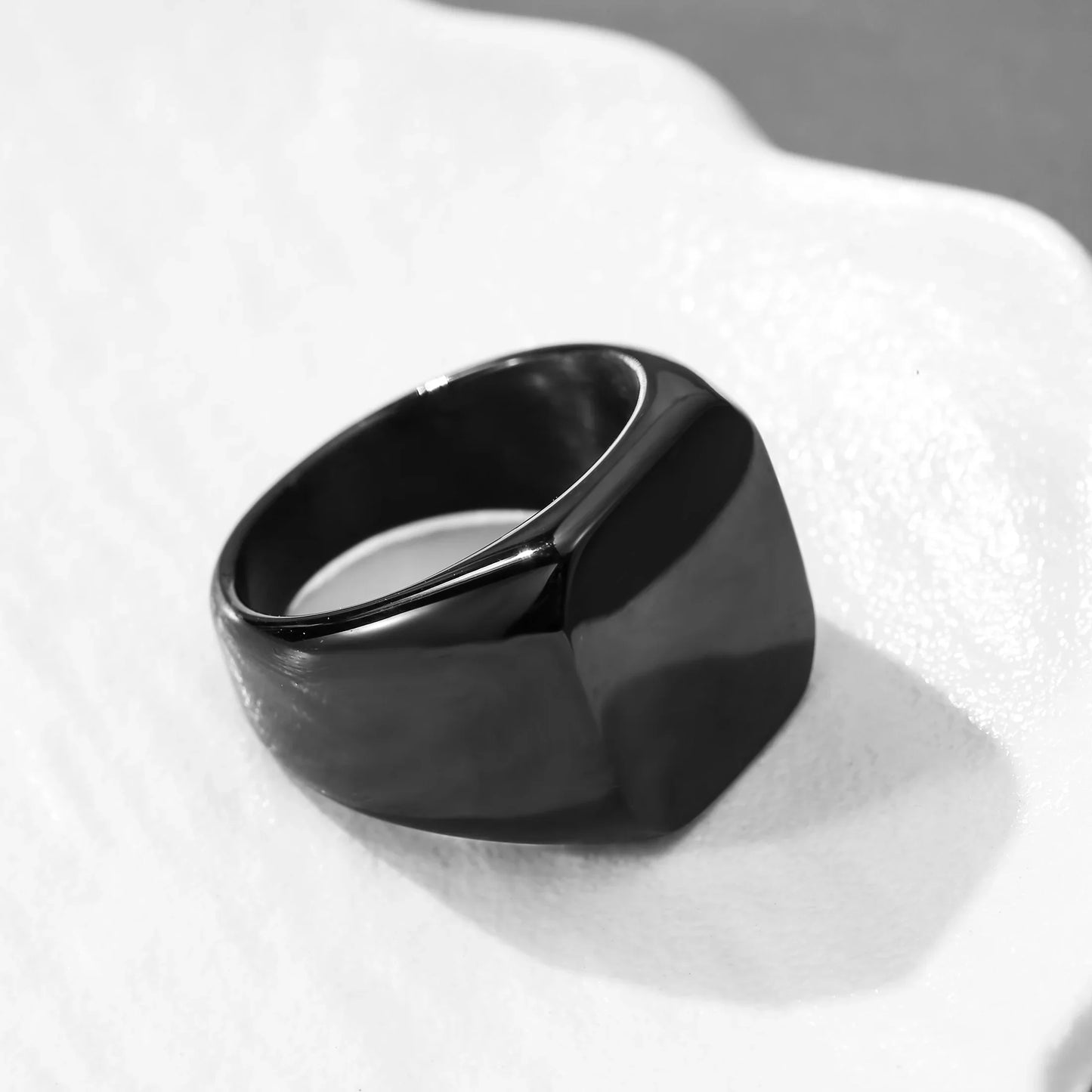 Sleek black minimalist signet ring with a polished finish on a white textured surface.