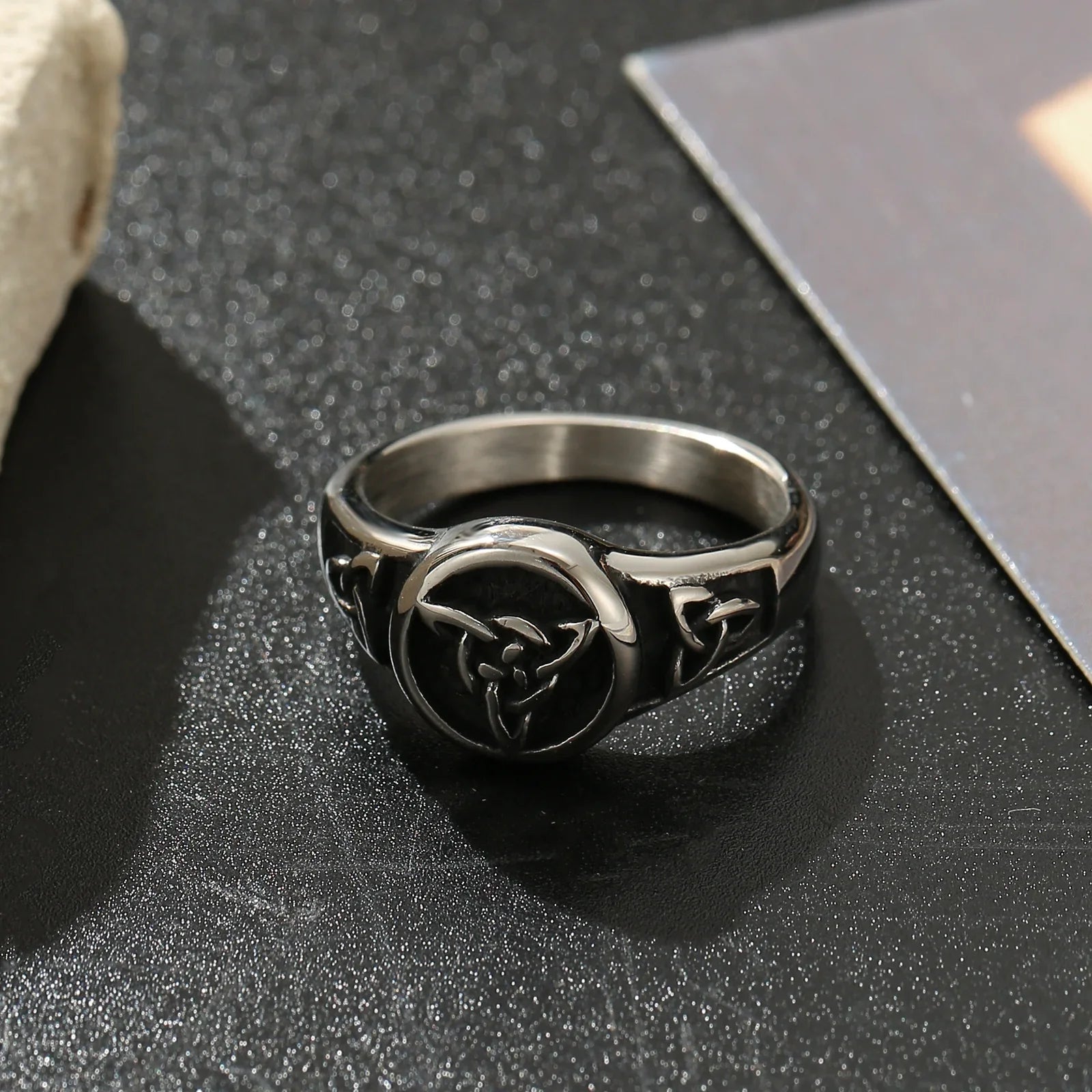 Stainless steel ring with engraved trinity knot design on textured black surface