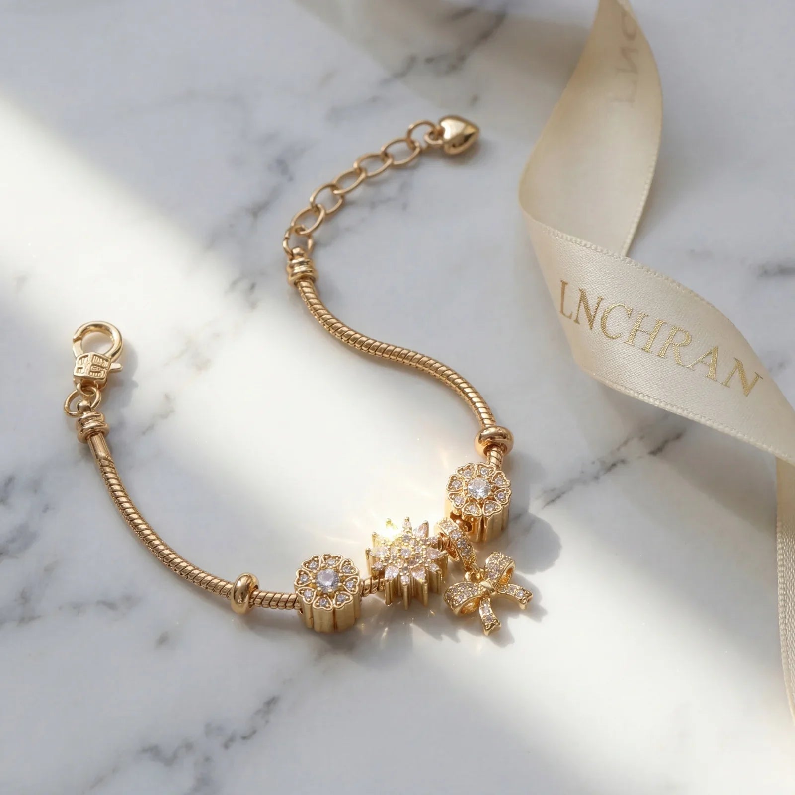 Gold charm bracelet with diamond accents on marble background, luxury jewelry style