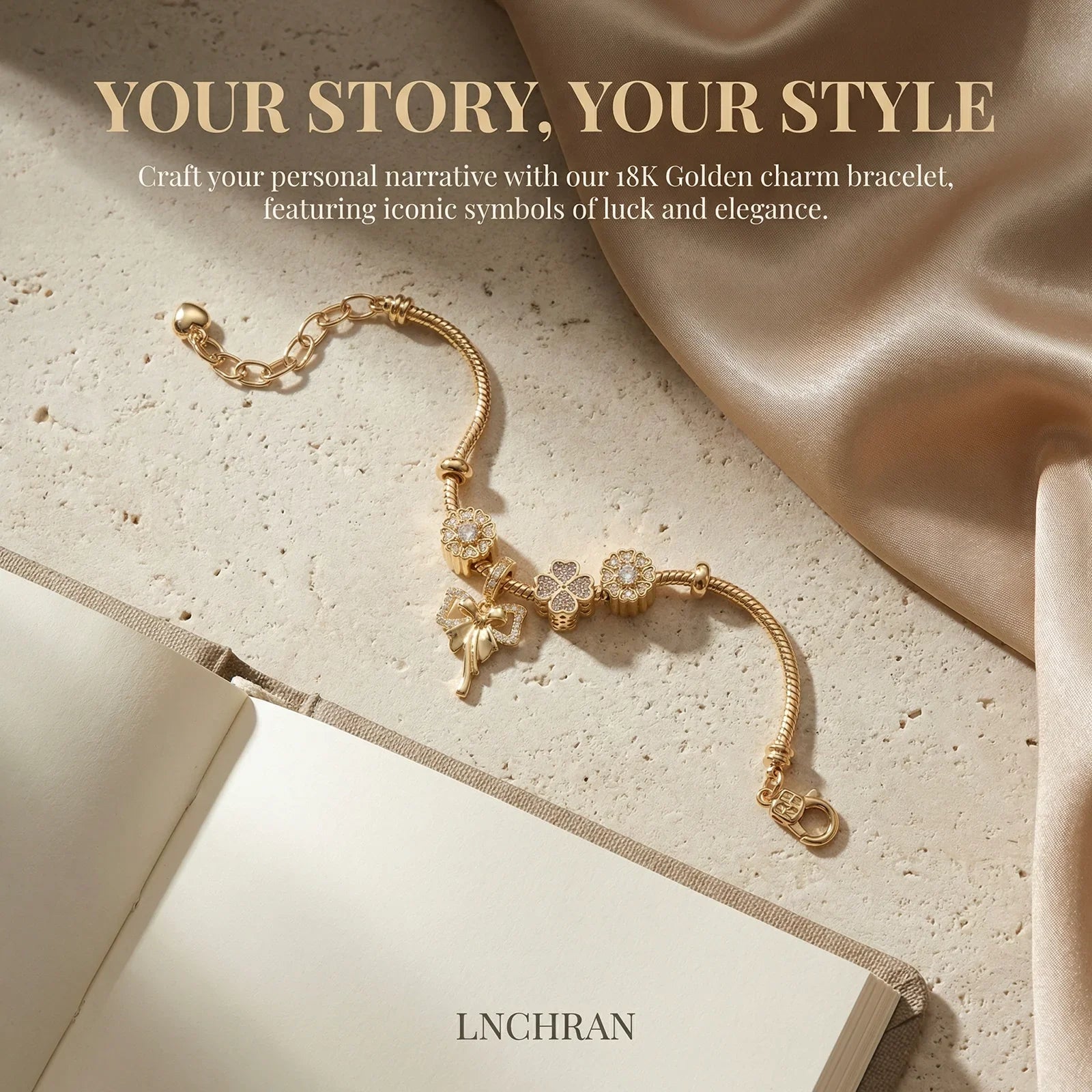 18K gold charm bracelet with floral and bow charms on a stone surface, next to a blank journal and champagne satin fabric, elegant jewelry flat lay.