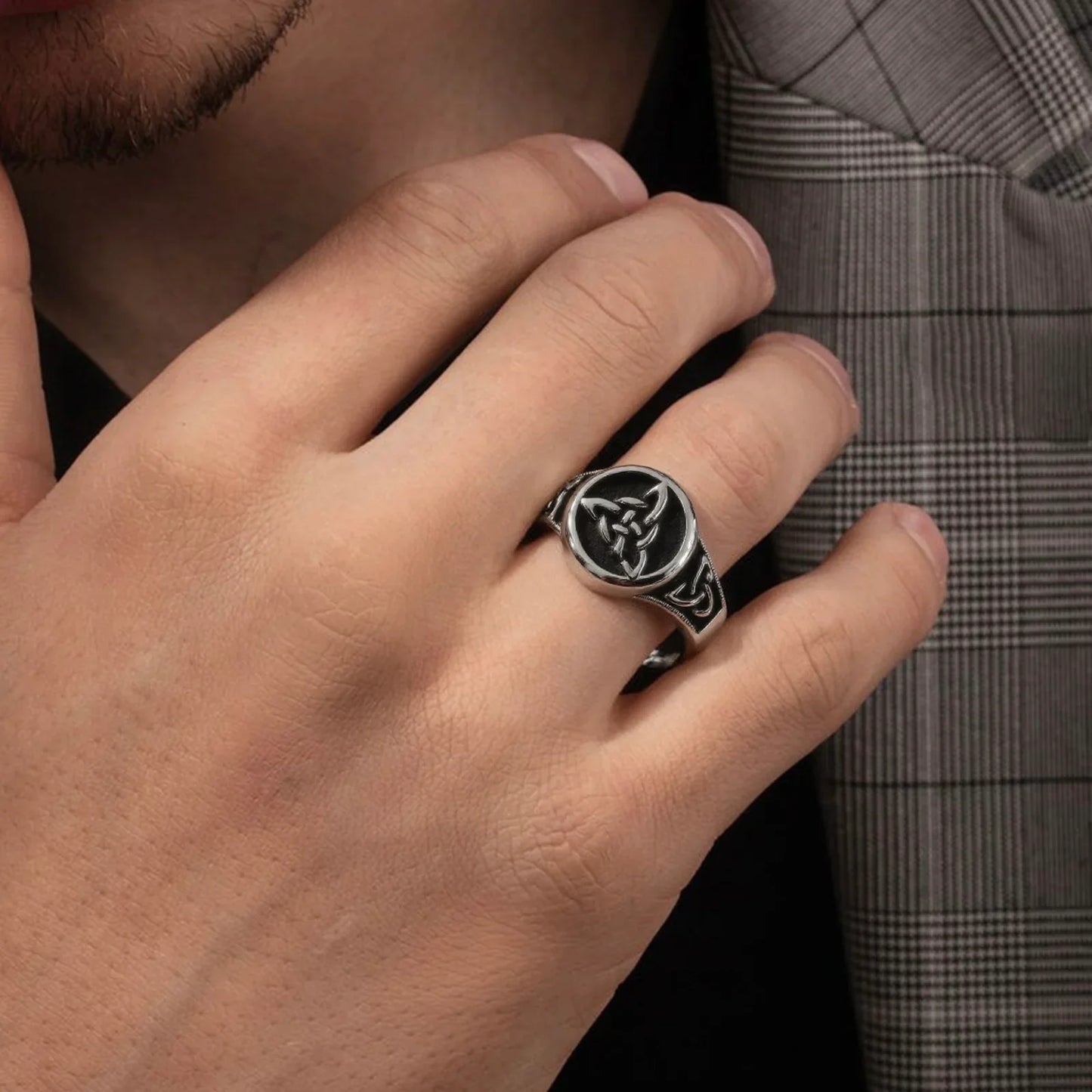 Man wearing a silver Celtic knot signet ring with engraved details on his finger.