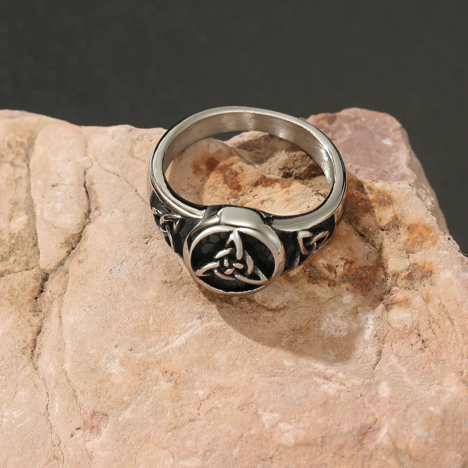 Stainless steel Celtic knot ring with black inlay displayed on a natural stone surface