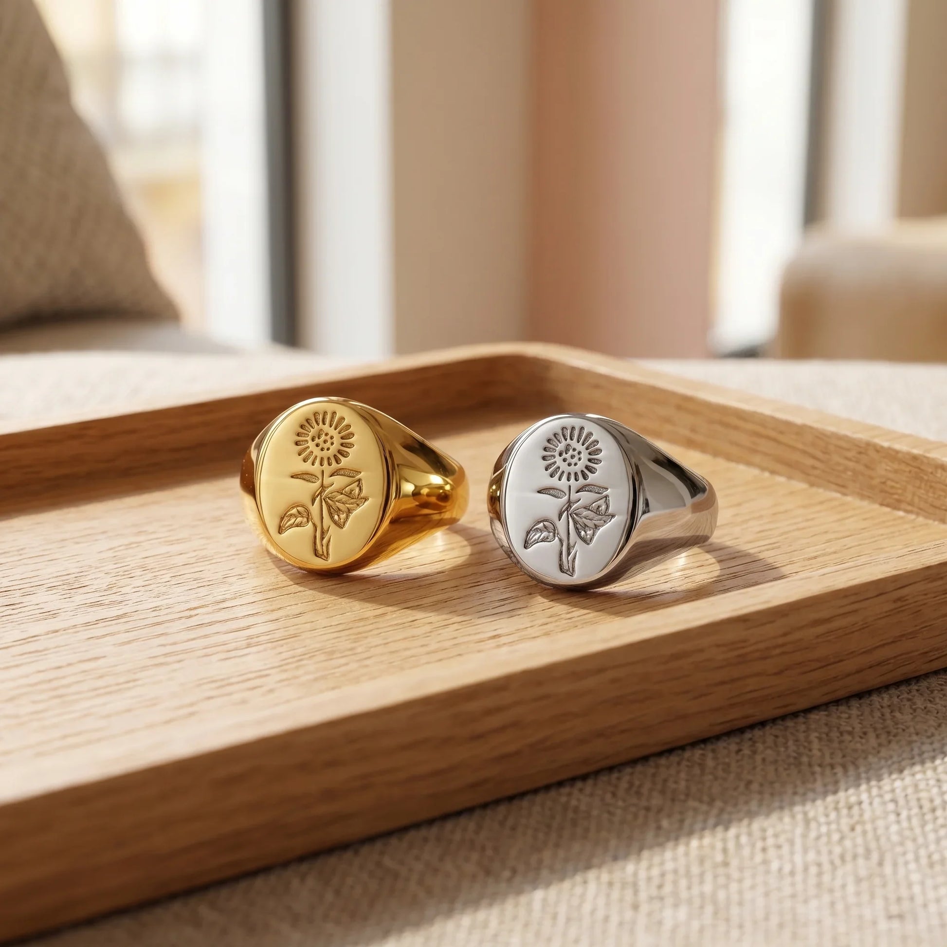Gold and silver floral signet rings with sunflower engraving on wooden tray, minimalist jewelry