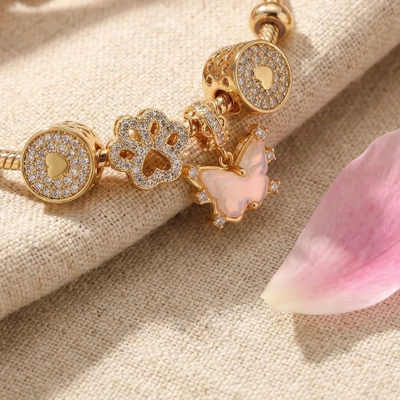 Gold charm bracelet with butterfly, heart, and paw print pendants on beige fabric