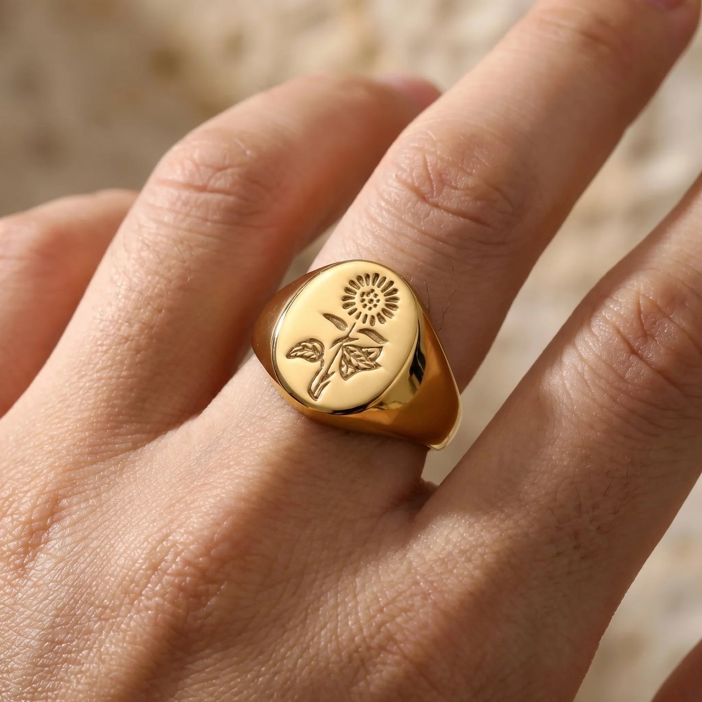 Gold signet ring with engraved sunflower design on hand, minimalist floral jewelry