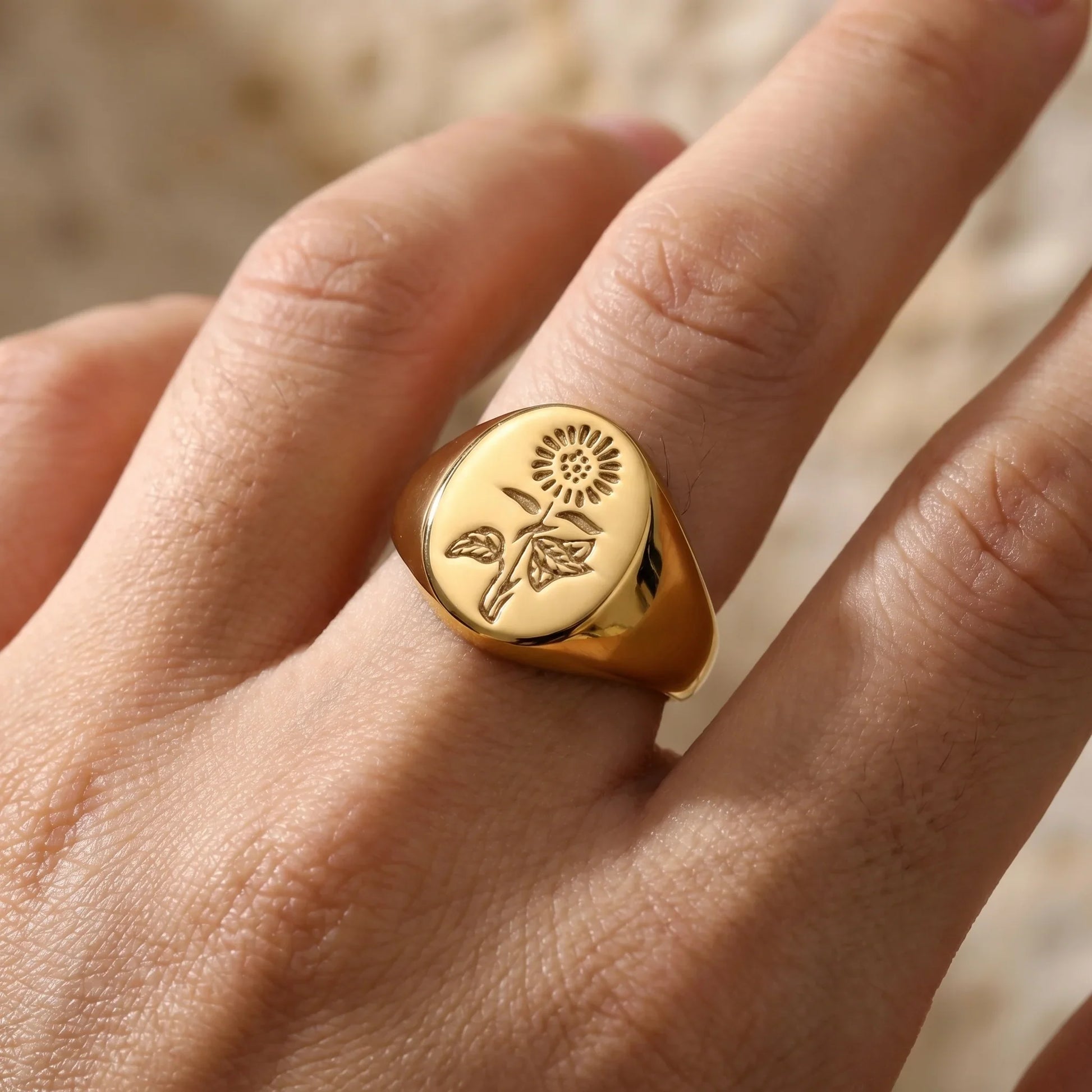 Gold signet ring with engraved sunflower design on hand, minimalist floral jewelry