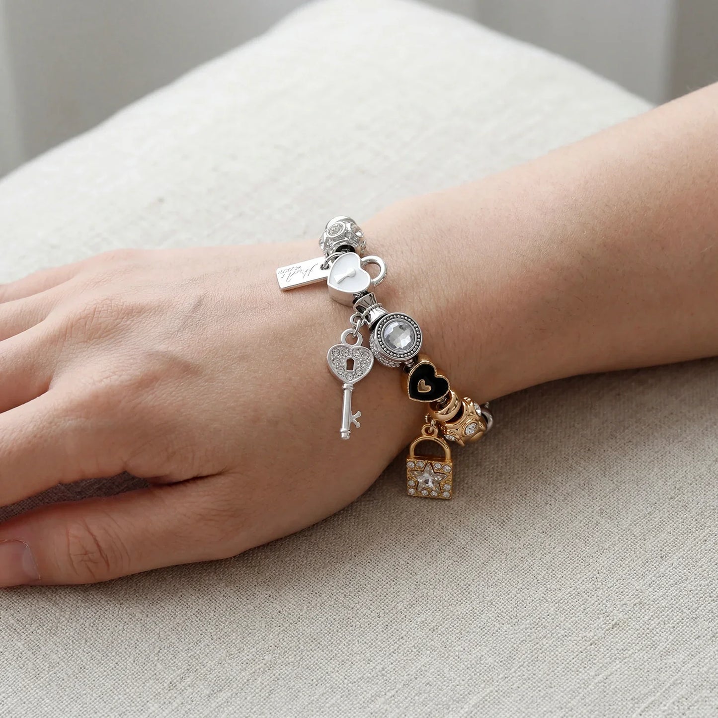Elegant charm bracelet with heart, key, and lock pendants in silver and gold on wrist