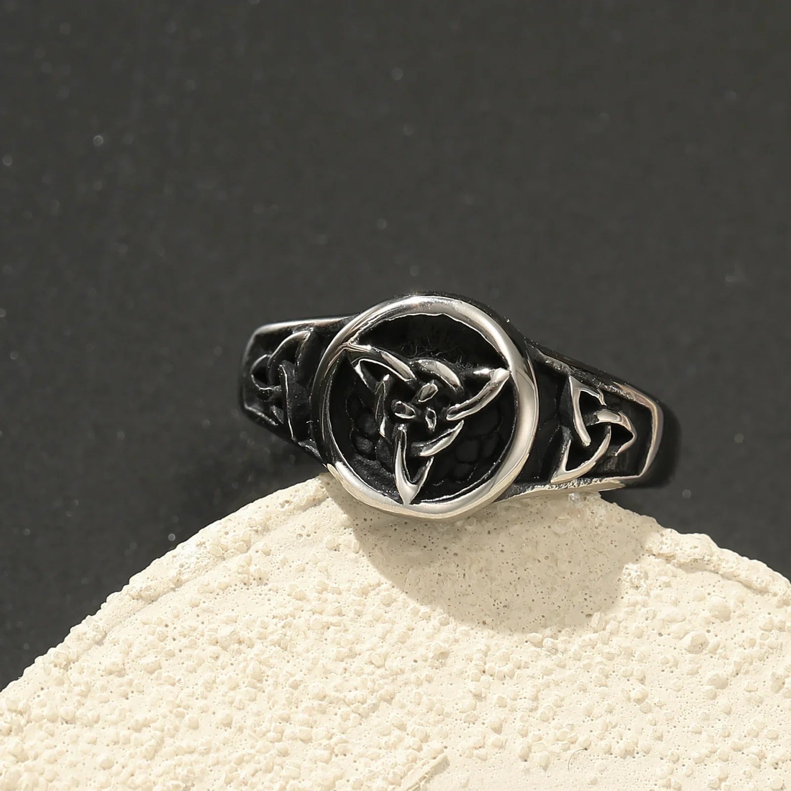Black and silver ring with Celtic knot design on round face, minimalist jewelry on stone.