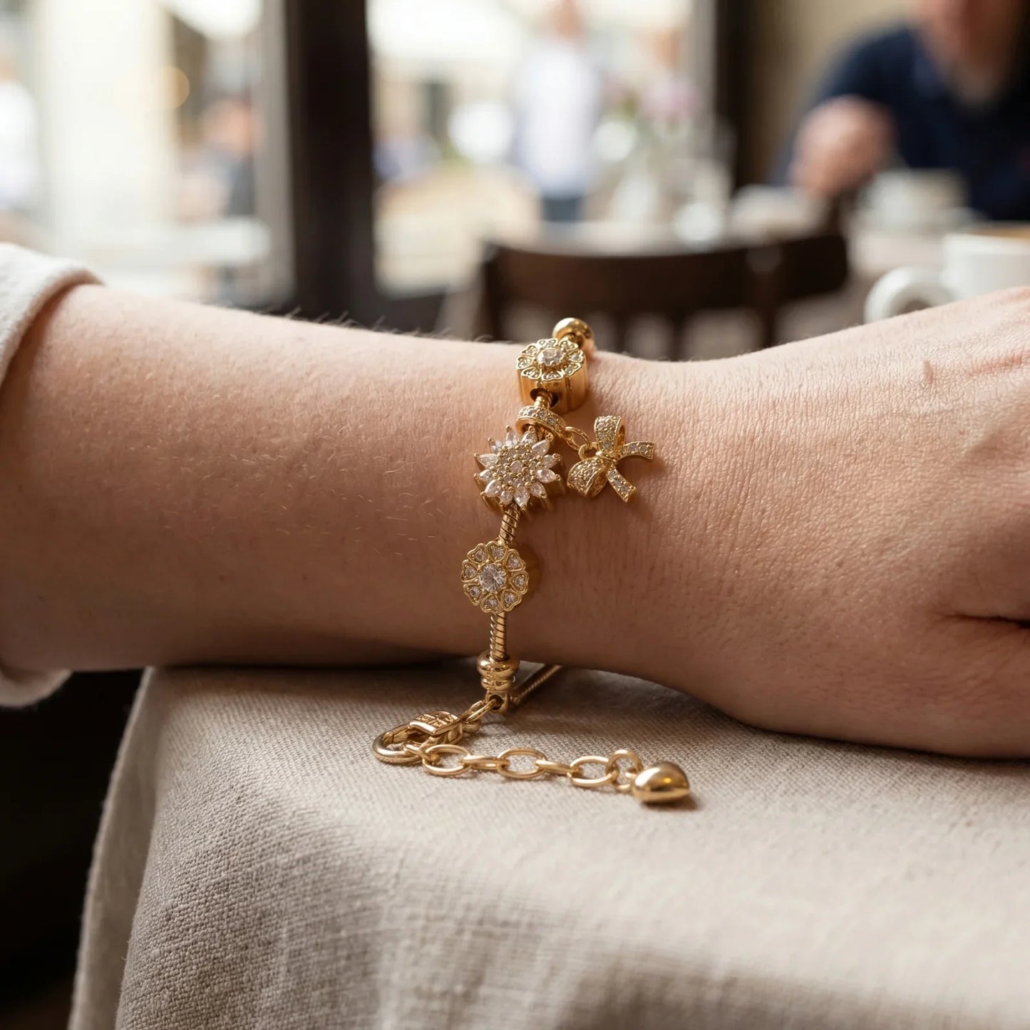 Hand wearing gold charm bracelet with flower and bow designs, modern elegant jewelry