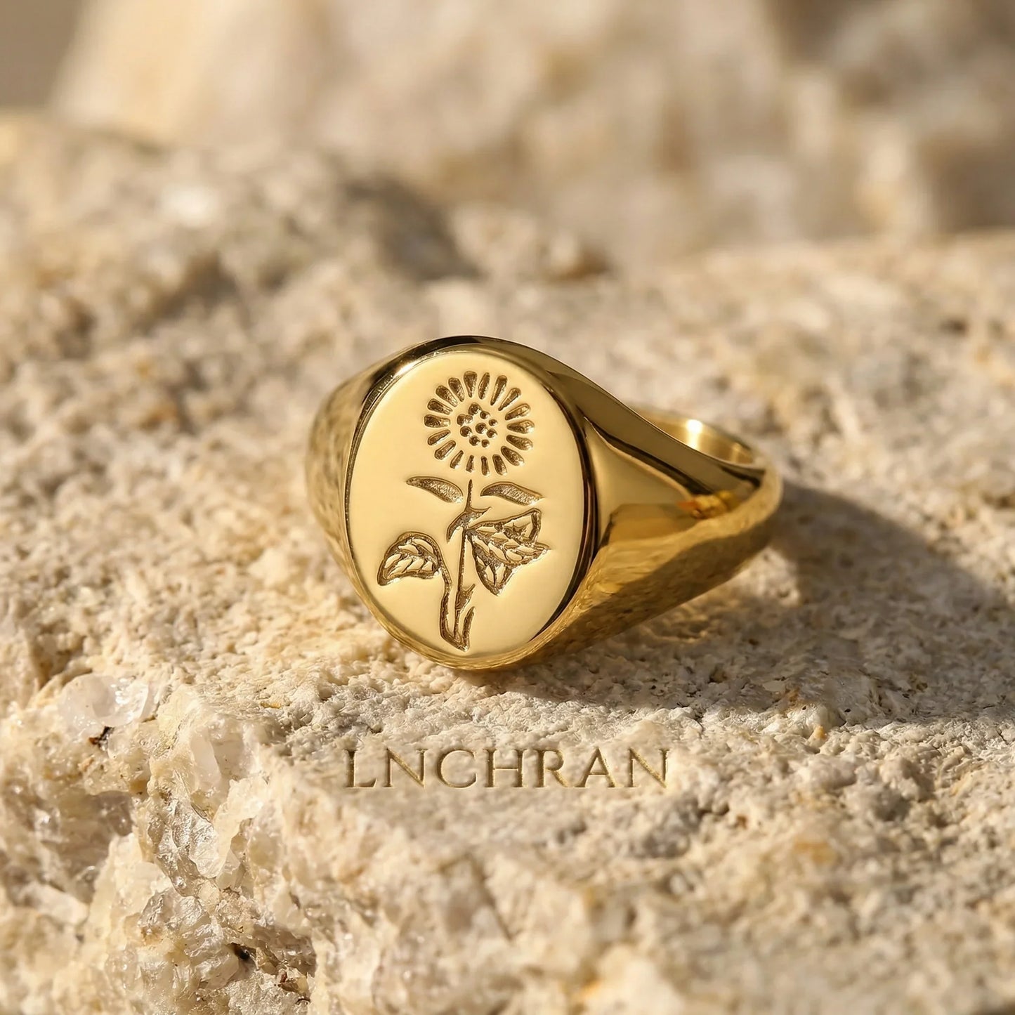 Gold signet ring with engraved sunflower design on textured stone surface