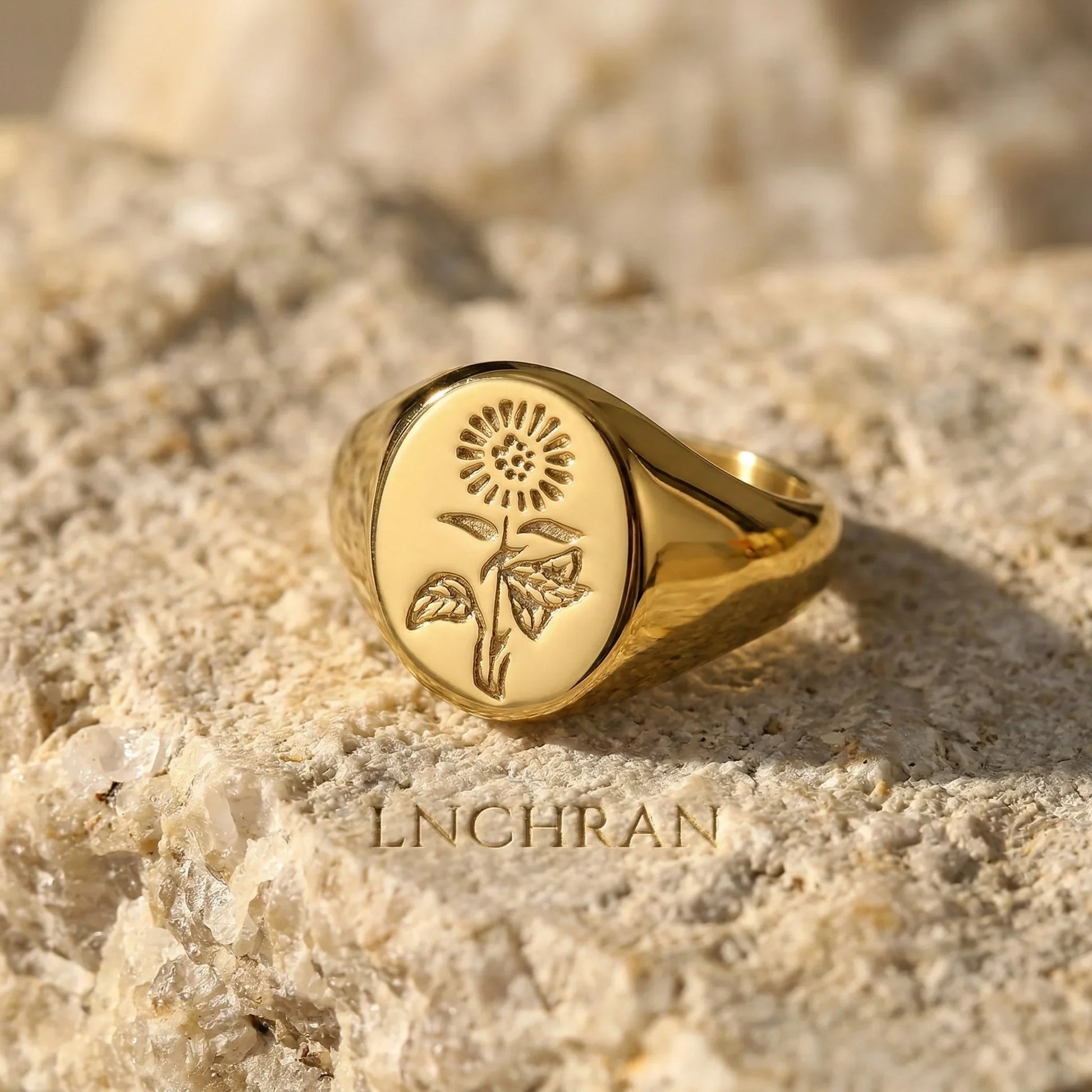 Gold signet ring with engraved sunflower design on textured stone surface