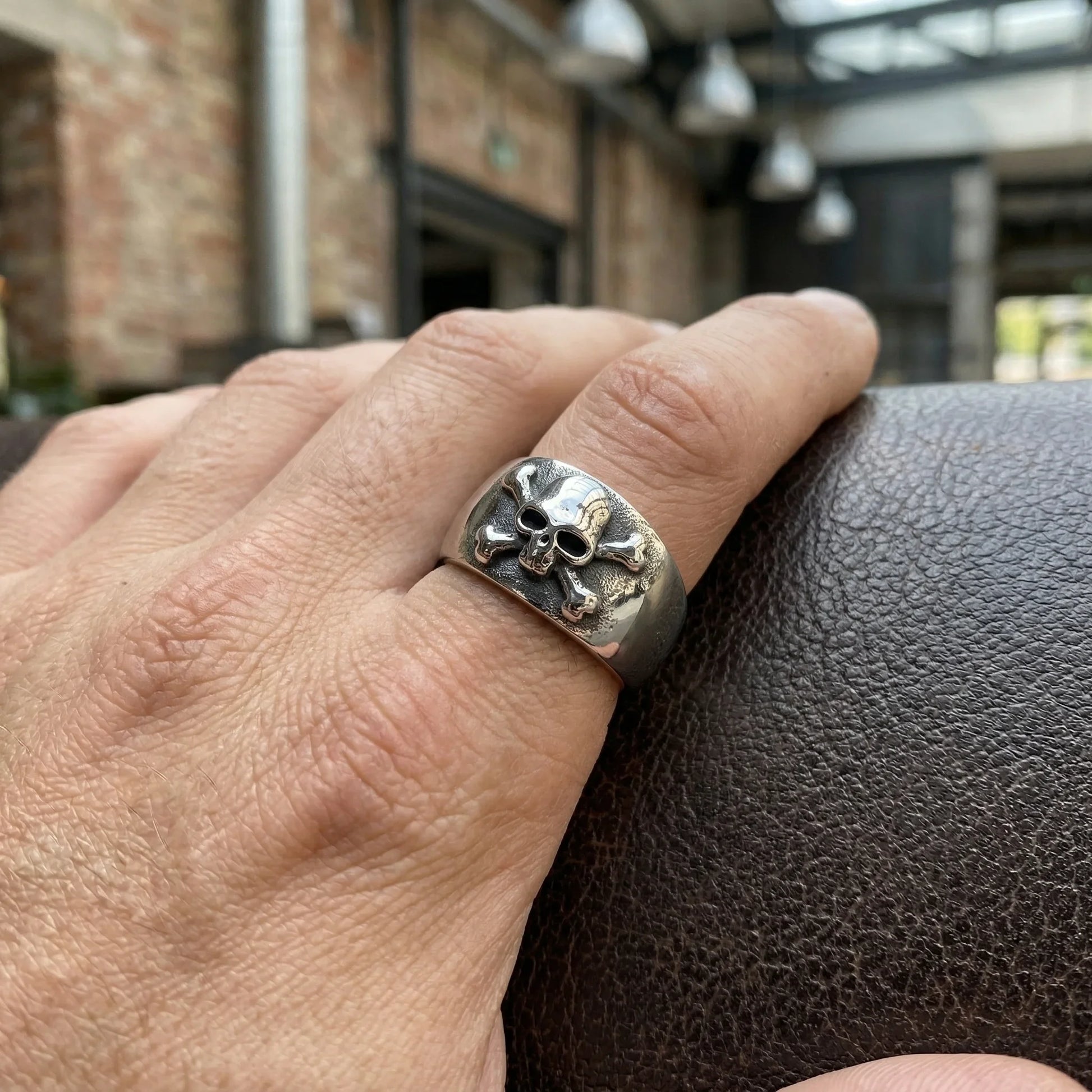Hand wearing a silver skull and crossbones statement ring, modern minimalist jewelry