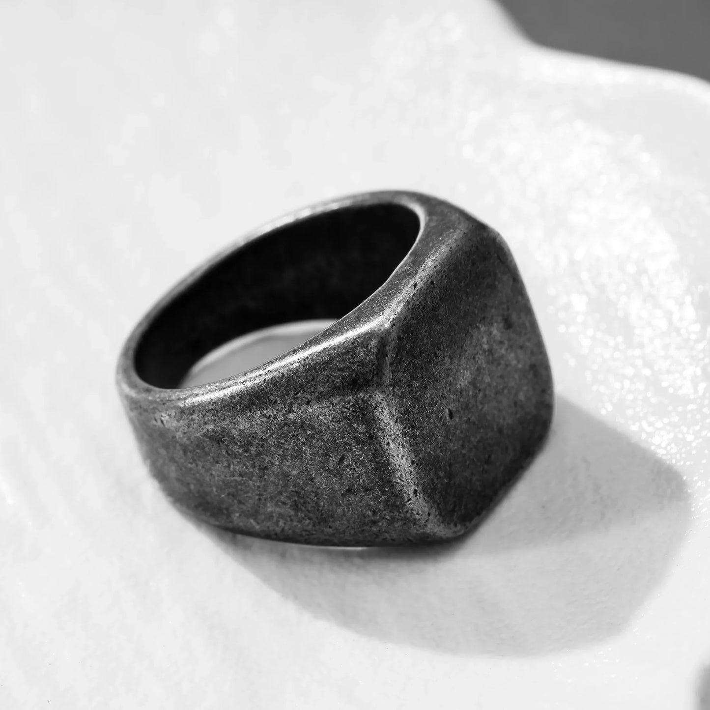 Minimalist square matte black signet ring on textured white surface