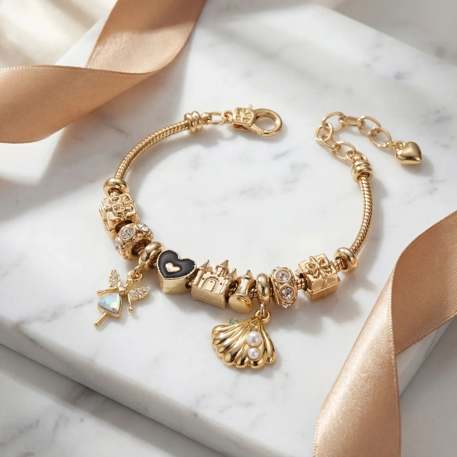 Gold charm bracelet with black heart, castle, shell, and gemstone charms on marble surface