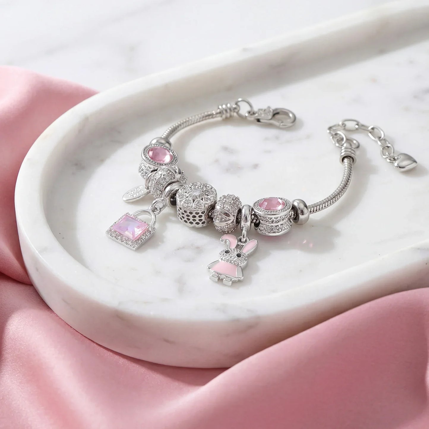 Silver charm bracelet with pink gemstones and bunny charm on marble tray with pink fabric