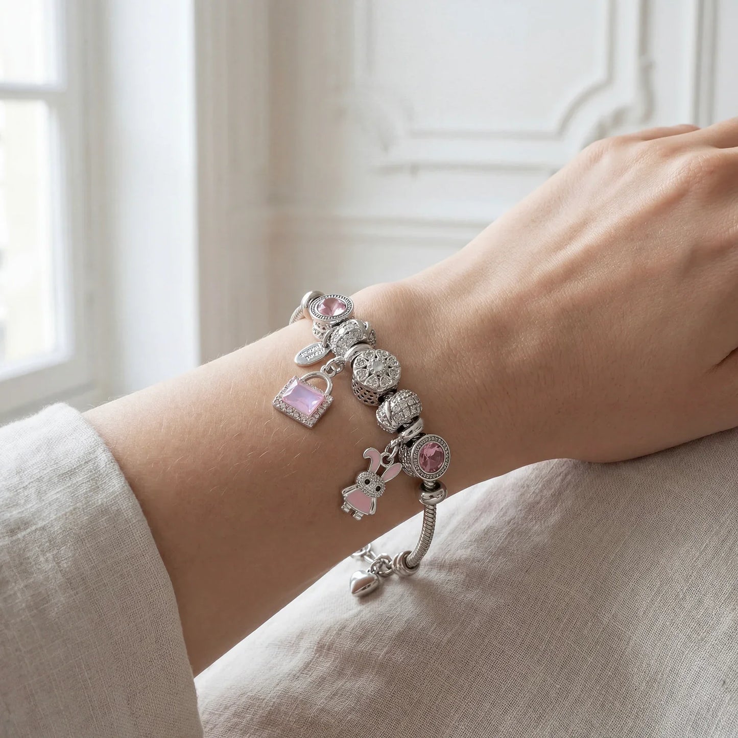 Elegant silver charm bracelet with pink gemstone and animal charms on a woman's wrist