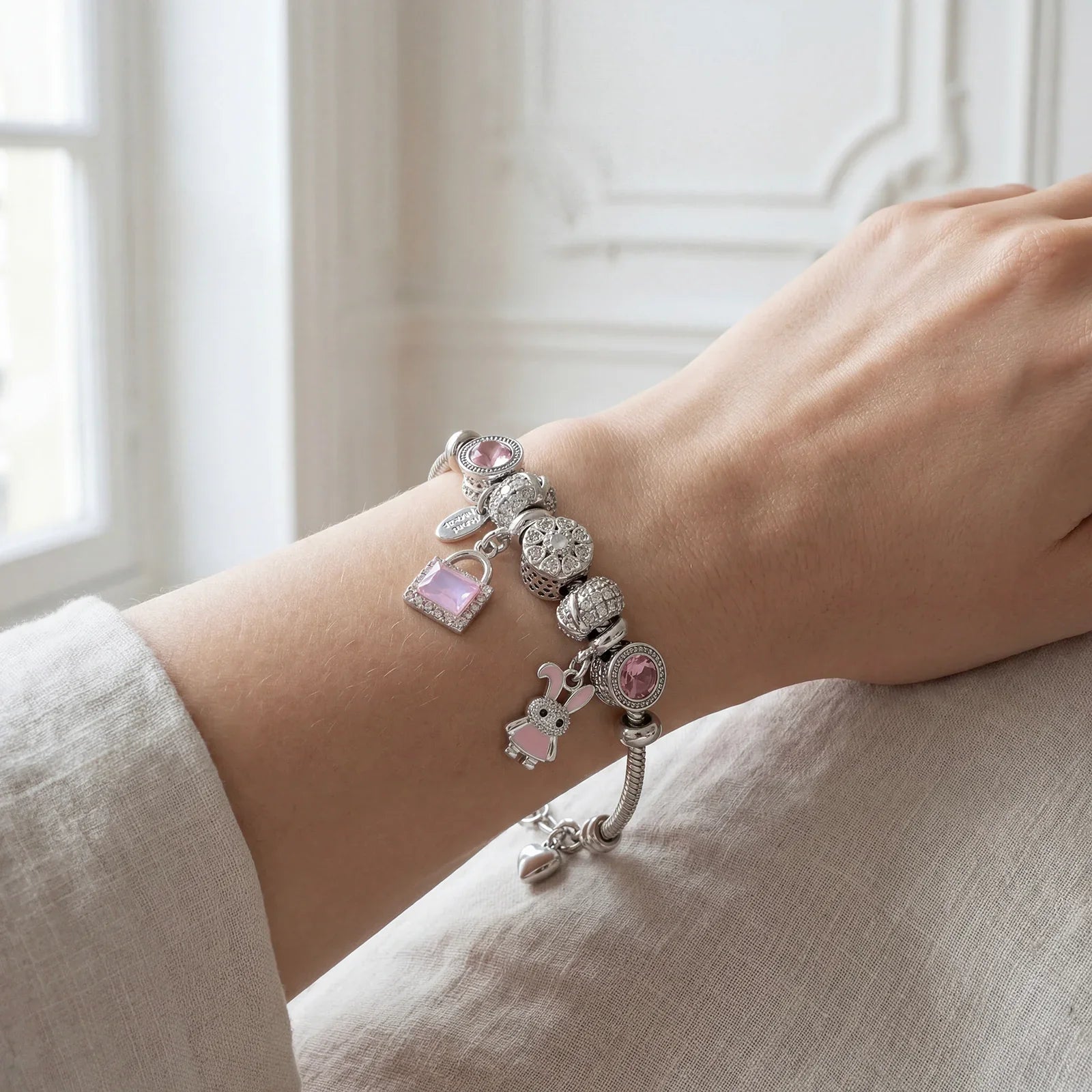 Elegant silver charm bracelet with pink gemstone and animal charms on a woman's wrist