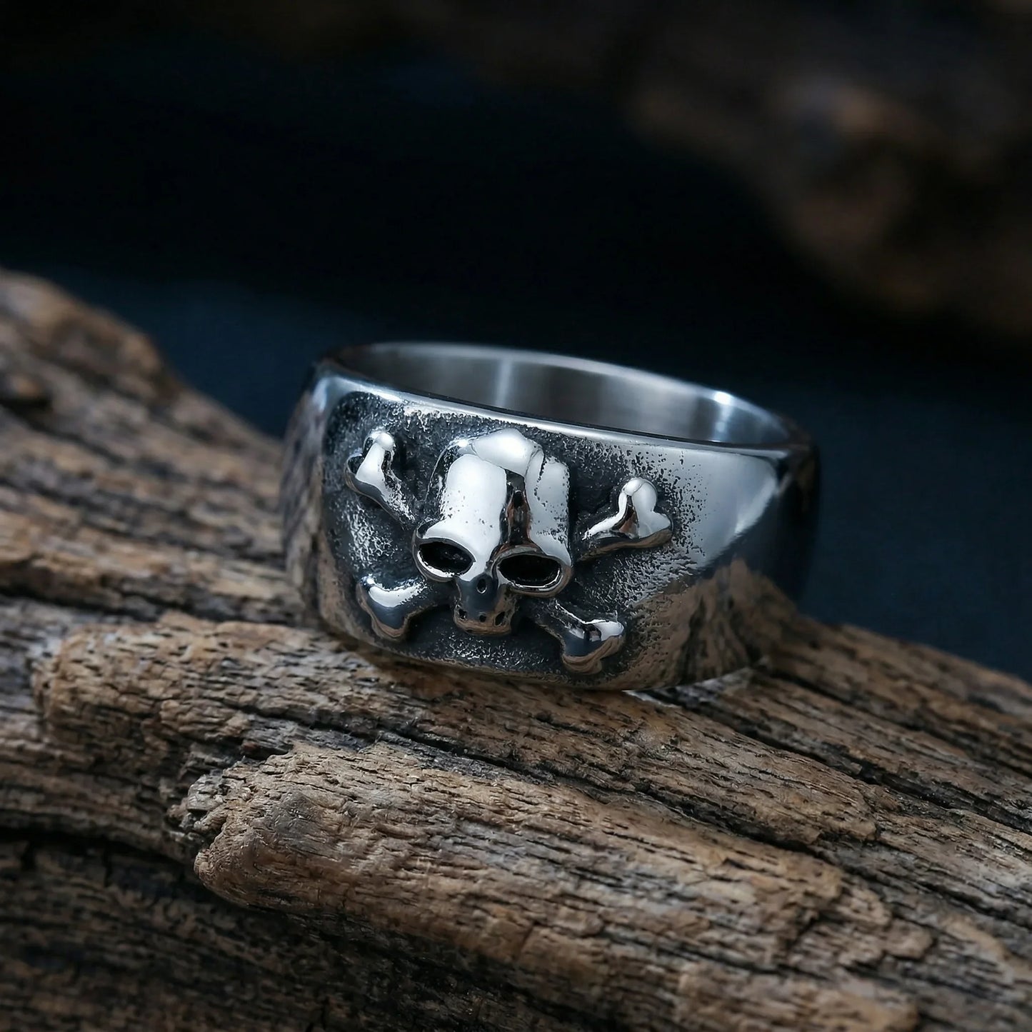 Men's silver ring with skull and crossbones design on textured band, displayed on wood